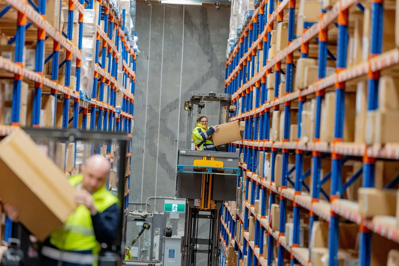 Warehouse operator taking packaged stock down from shelving for controlled handling